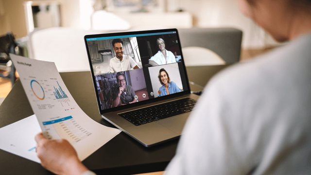 A group of people are on a video conference, talking with someone off the screen who is holding a report in one hand.