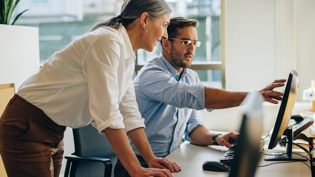 Image of woman standing at desk with male coworker working with technology.