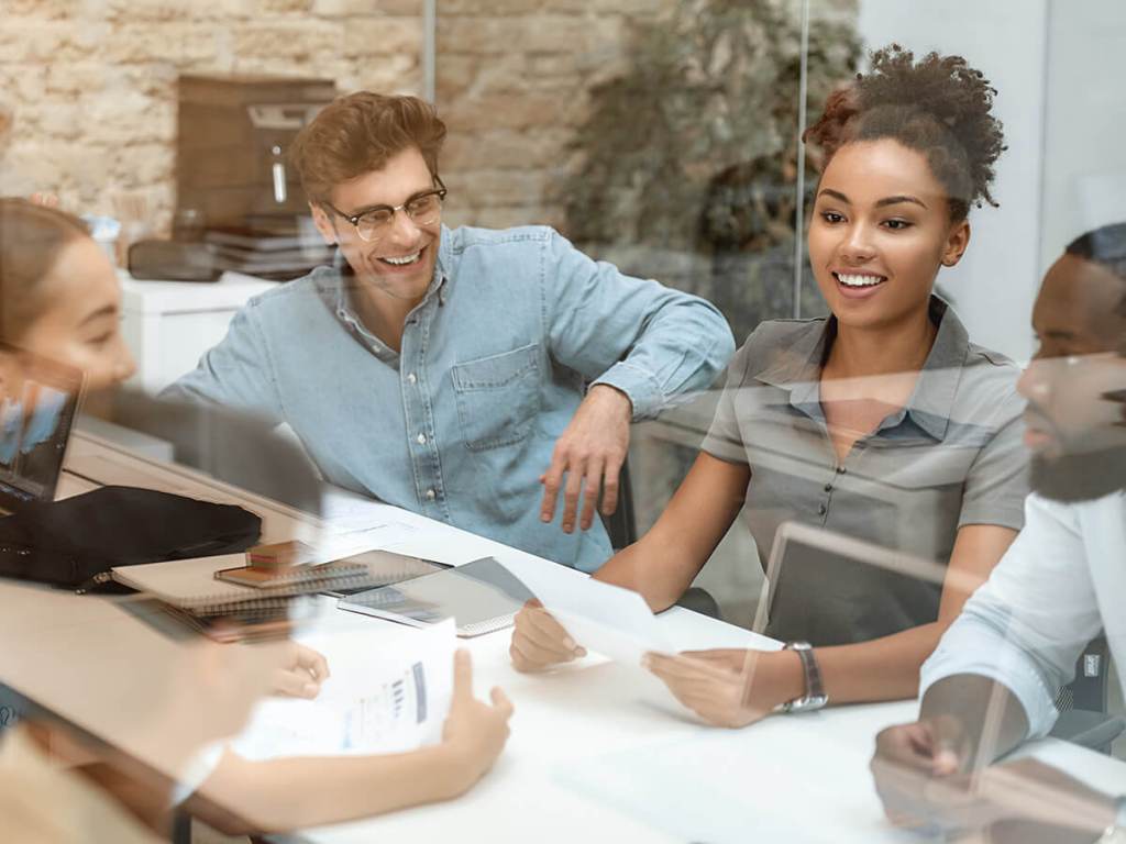 A group of coworkers, with a diverse set of skills amongst them, sit around a table in a conference room.