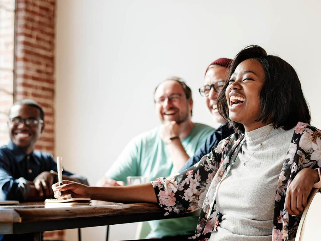 Image of four adult co-workers sitting joyously around a conference table in an office because they did their tax season checklist for accounting firms.