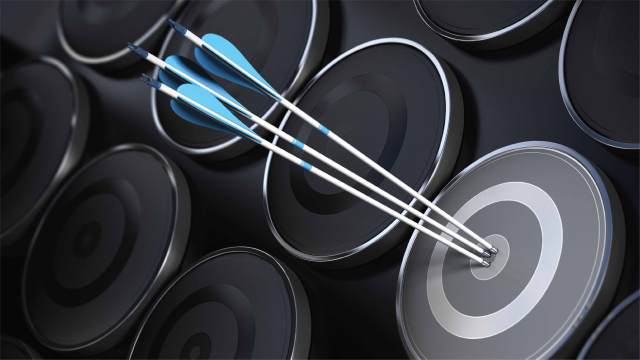Multiple black targets are posed next to each other on a black background. Three blue-tipped and feathered arrows crowd the bullseye of the highlighted target.