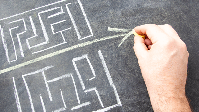 An image of a chalkboard background, with a maze drawn in white chalk. A clear path through the maze is defined by a yellow chalk line shaped like an arrow.