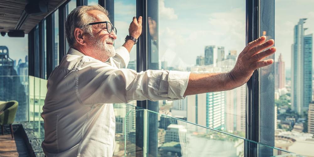 An image of an older man standing at an office window, looking over the cityscape.