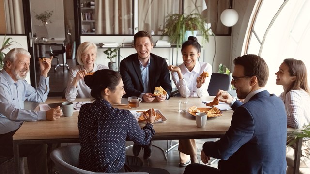 A group of people sit around a table, eating and visiting, looking happy to be celebrating the end of tax season.