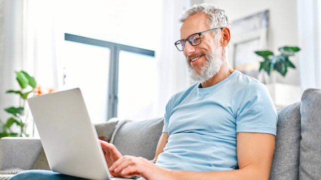 A man sits on a sofa in front of a laptop, smiling at his remote coworkers as they relax and recap tax season.