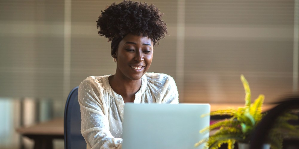 A woman sits in front of a laptop working. She smiles as she narrows down her options for QuickBooks hosting providers by asking the right questions.