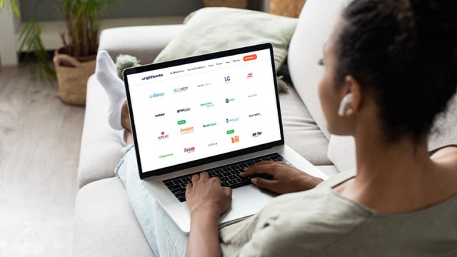 A woman sits on a sofa, looking at a laptop with a group of applications on the screen, all hosted within the same intelligent cloud platform from Rightworks.