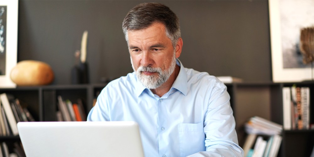 An older gentleman sits in his office, looking at a laptop as he considers where his accounting firm fits on The Modern Firm Maturity Continuum.