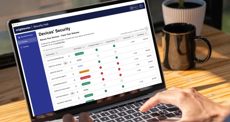 Laptop displaying a Devices’ Security dashboard with device status indicators, viewed on a desk beside a coffee mug.