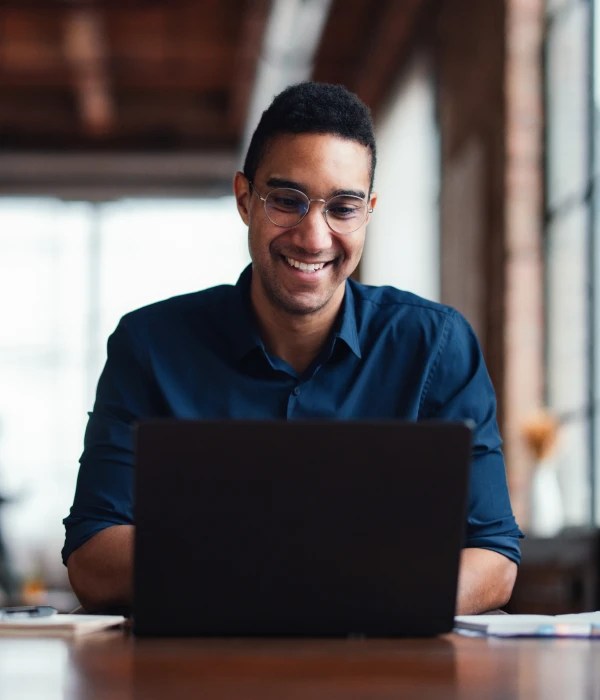 Person wearing glasses seated at a desk, working on a laptop in an office setting.
