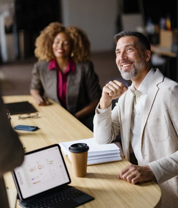 Professionals seated at a conference table with documents, a tablet, and a takeaway coffee cup.