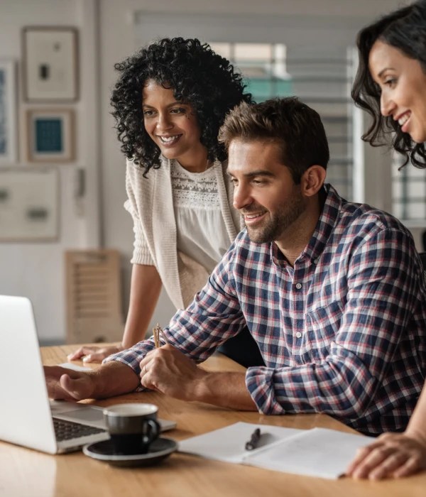Three people collaborating around a laptop at a table with documents and a coffee cup