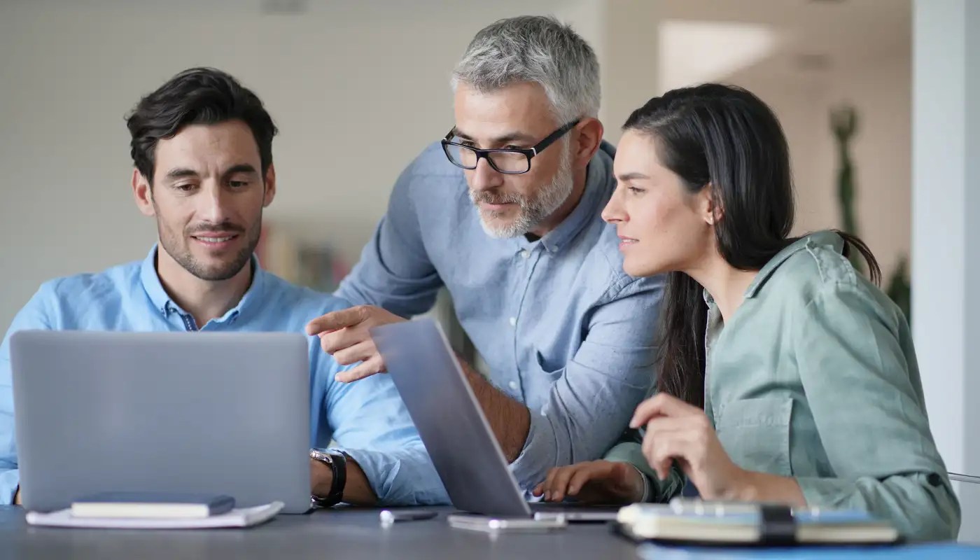 Three people collaborating with two laptops at a table